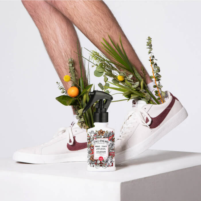 Legs in sneakers with plants growing out, accompanied by a stylish spray bottle on a white platform, create an imaginative and whimsical tableau.