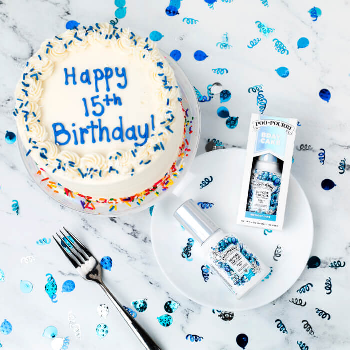 A round cake with Happy 15th Birthday text is surrounded by blue confetti and a fork. A festive Poo-Pourri gift set accompanies it on the plate, adding a touch of fun to the celebration.