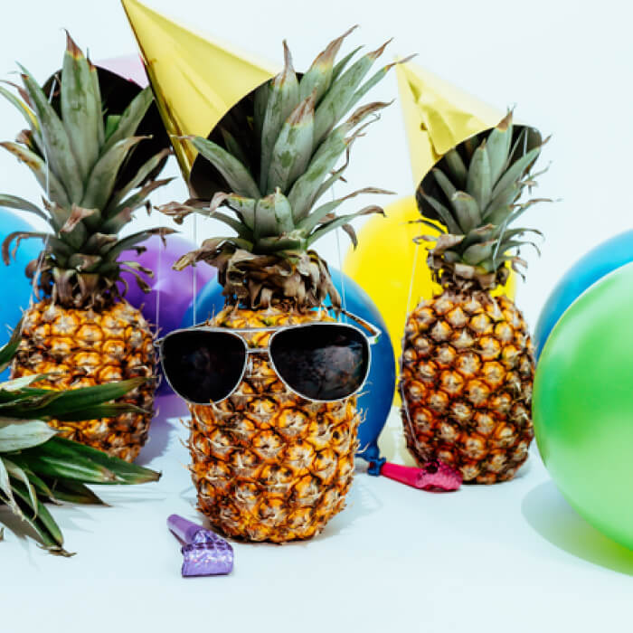 A pineapple wearing sunglasses, surrounded by balloons and party hats, sets the stage for a vibrant celebration.
