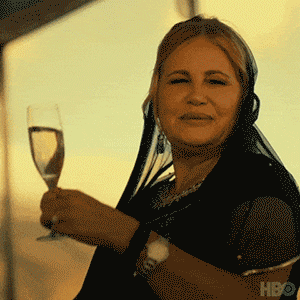 A person in black attire holds a champagne glass, smiling serenely as the golden sunset paints the sky.