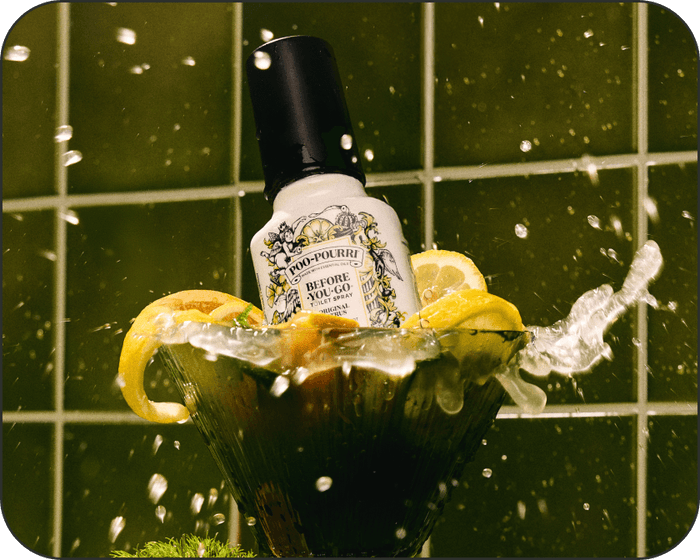 Bottle of Poo~Pourri Original Citrus toilet spray with lemons in a bowl on a green tiled background