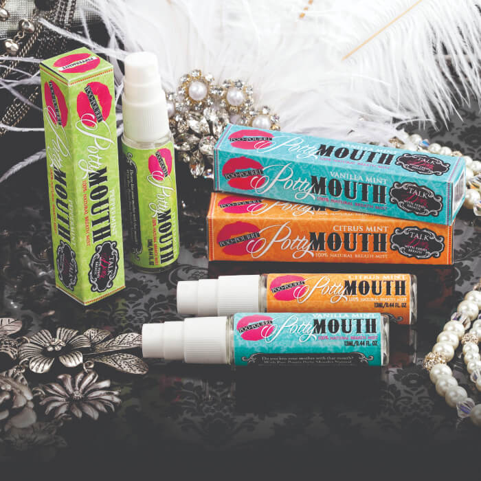 The vibrant mouth spray packaging sits on a patterned surface adorned with decorative feathers and sparkling jewelry, creating an enticing display.