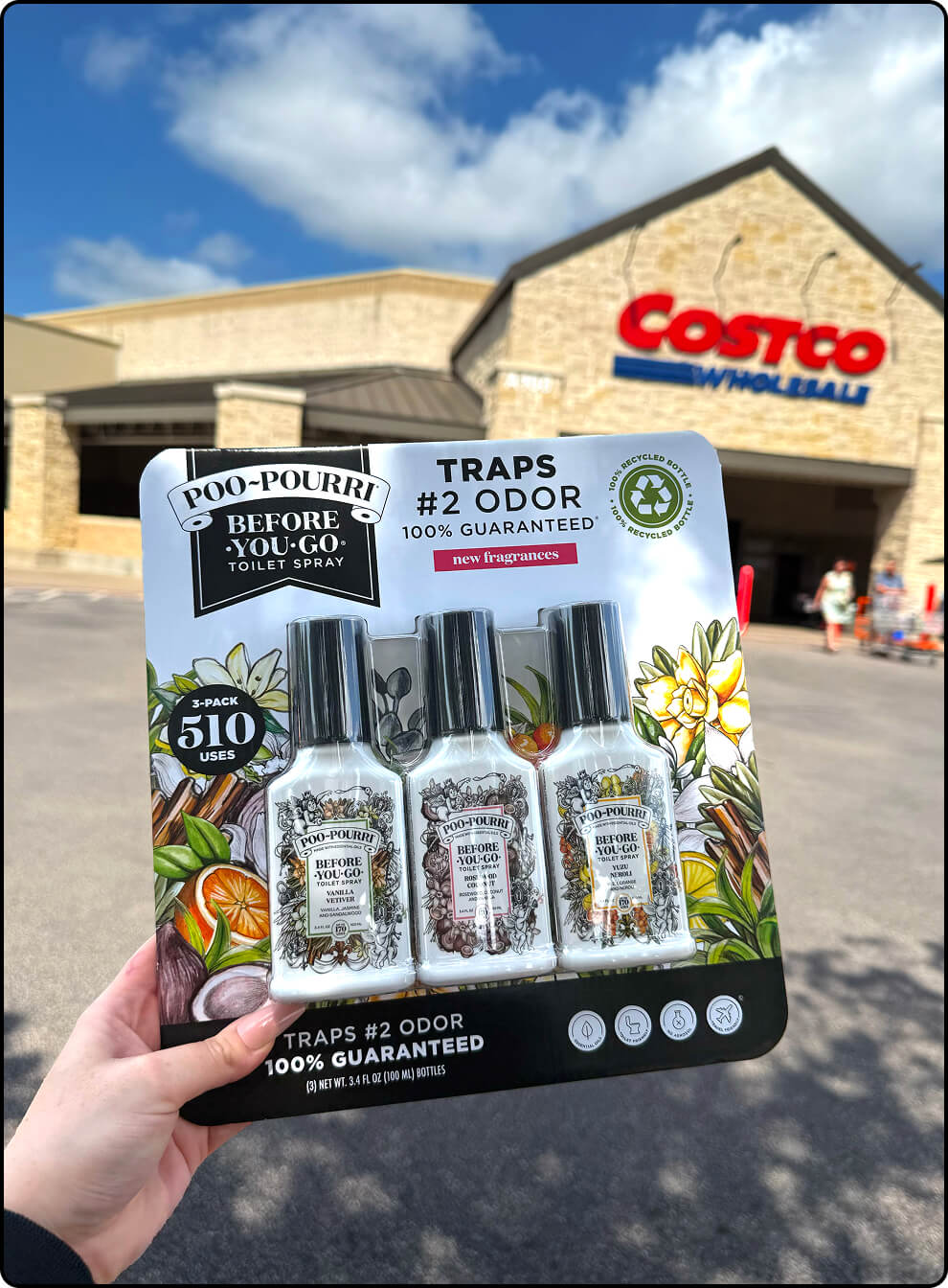 Poo-Pourri 3-pack with Vanilla Vetiver, Rosewood Coconut, and Yuzu Neroli, held in front of a Costco store.