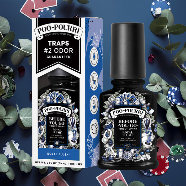 A ~Poo-Pourri “Before You Go” toilet spray in the Royal Flush scent is displayed alongside its packaging against a decorative dark blue background, featuring plants, cards, and poker chips. The bottle and box have an intricate design with tuxedos, toilet paper, cards, and dice. The packaging emphasizes the product’s ability to trap odors before they start, with key details such as “100 Uses,” “No Aerosols,” and “Essential Oils” visible.