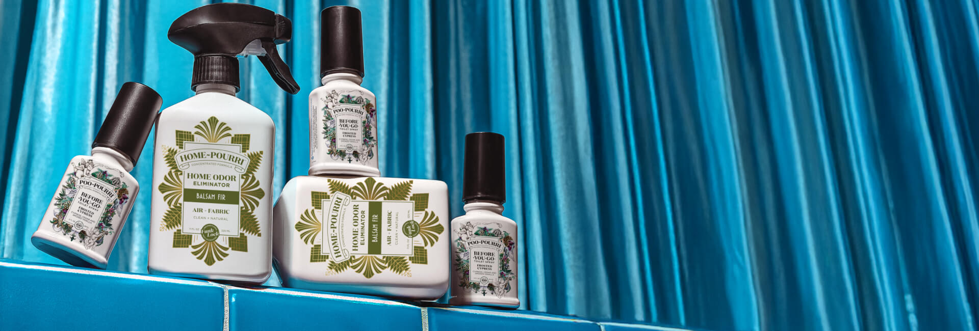 Set of Poo and Home Pourri products on a blue tiled surface with a blue curtain background