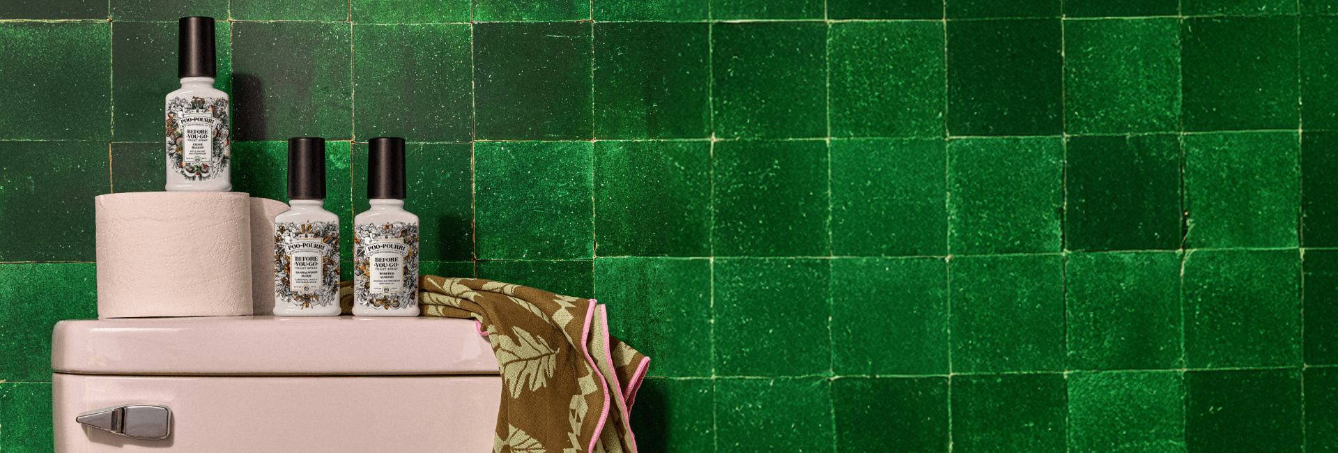 Poo~Pourri fall scented products on top of a toilet against a green tiled wall
