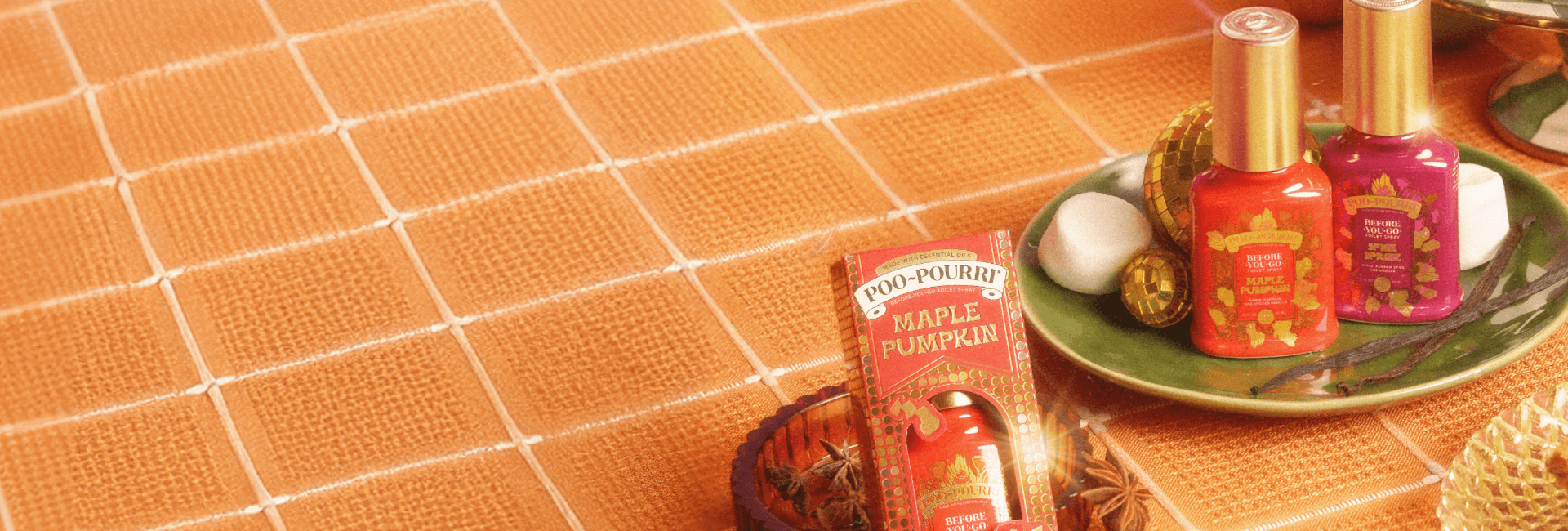 Table setting with fall scented Poo~Pourri bottles, pumpkin pie, apples, and decorative fall items against a pink wall.