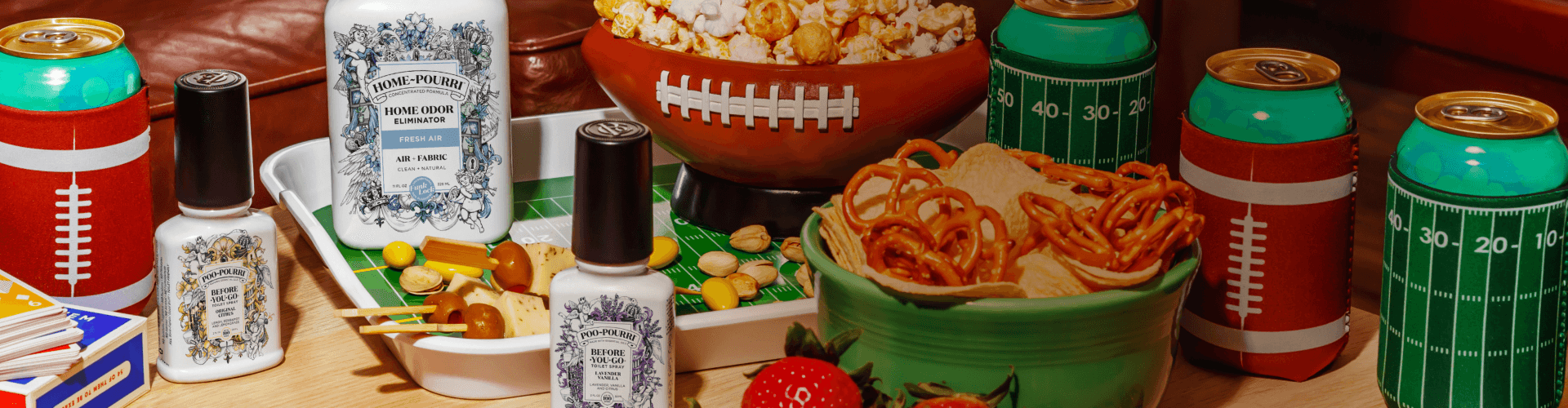 Poo~Pourri and Home~Pourri spray bottle with football-themed snacks and drinks on a table with decorative items.