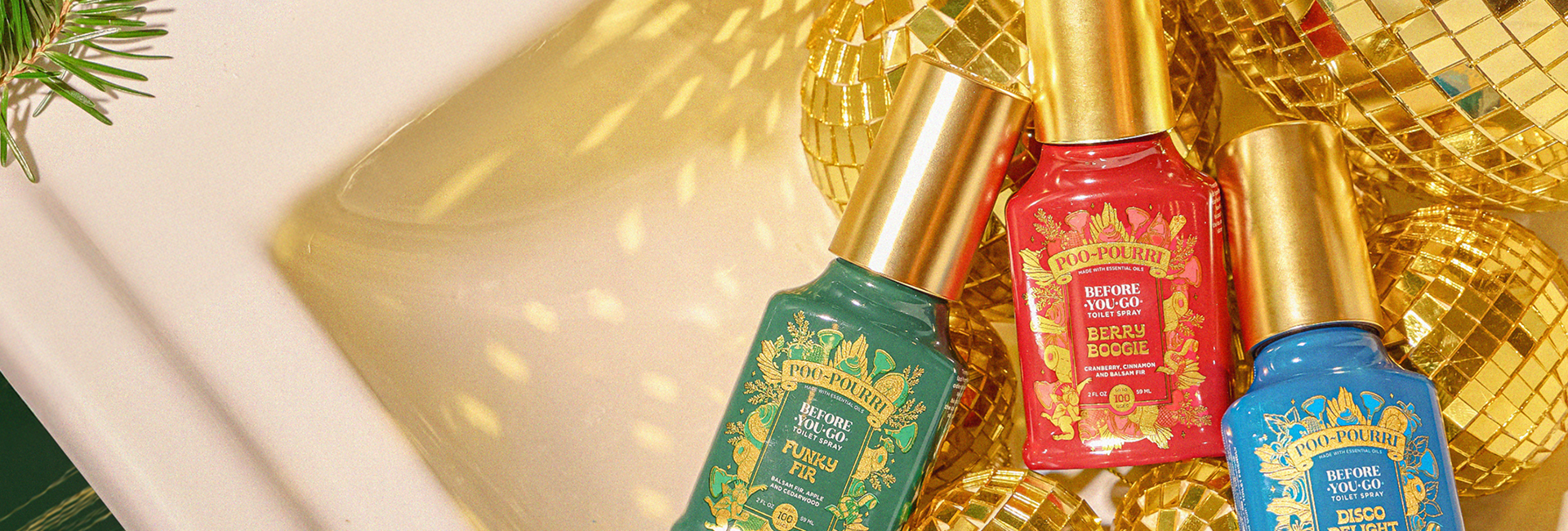 Poo~Pourri Funky Fir, Berry Boogie, and Disco Delight spray bottles inside a sink with golden disco balls.