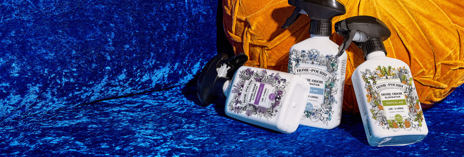 Three bottles of Home~Pourri on a blue textured background and an orange textured pillow