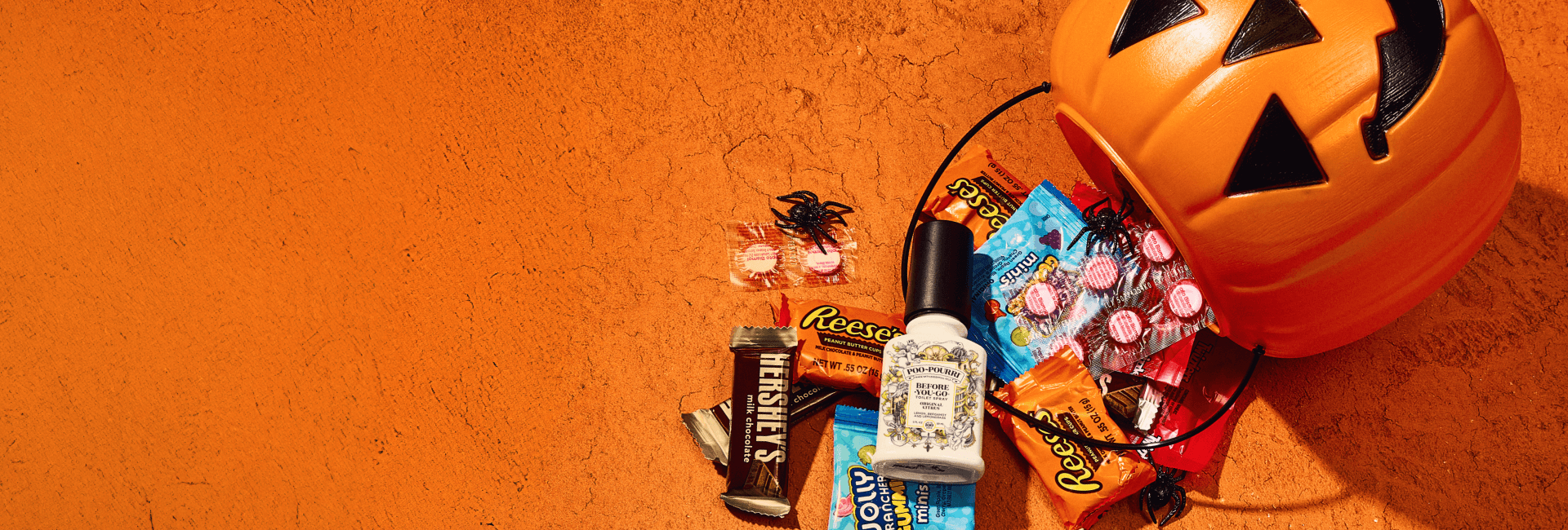 Poo~Pourri spray bottles with Halloween themed candy on a textured orange surface