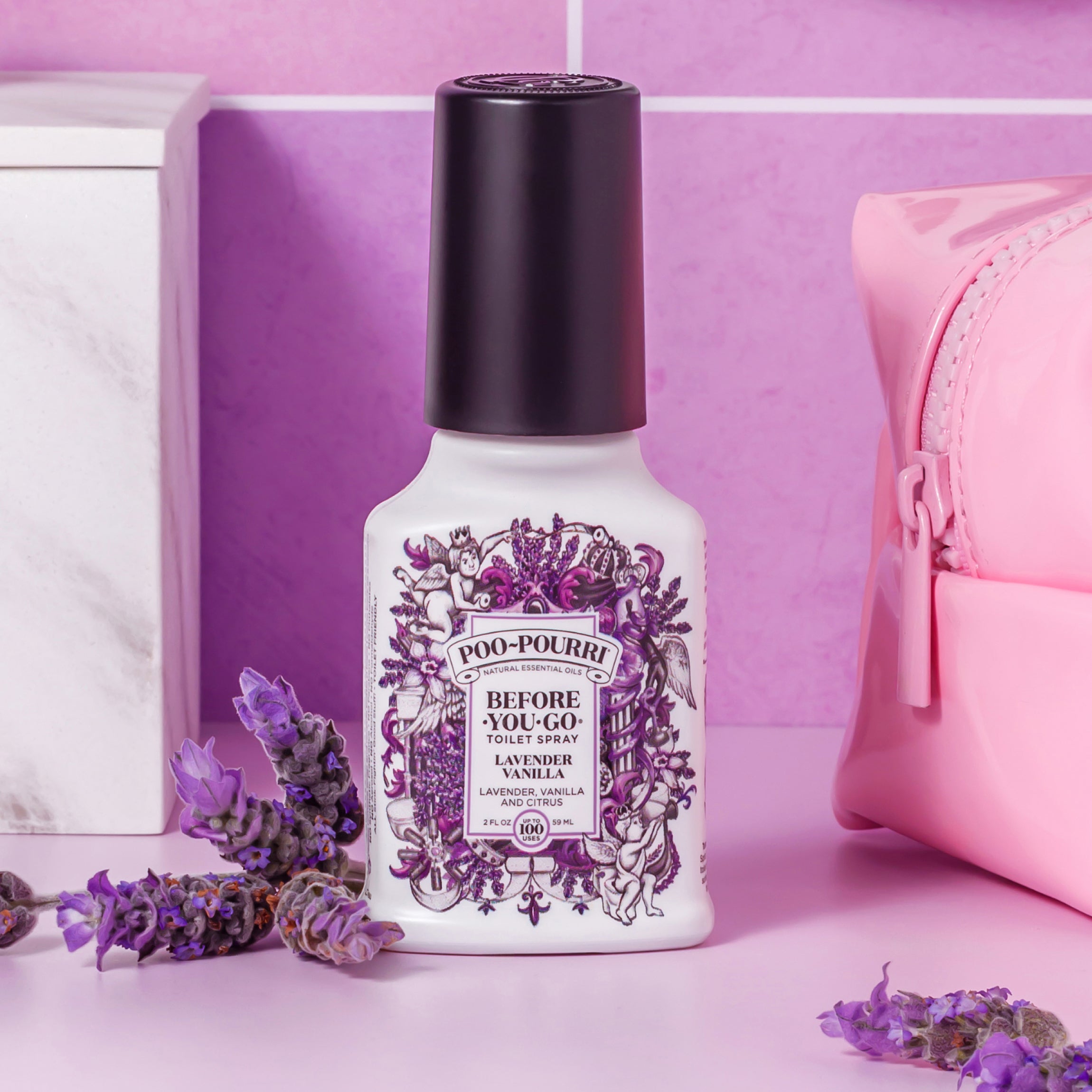 A bottle of Poo~Pourri toilet spray, features intricate black and purple designs with cherubs, and the label indicates a lavender vanilla scent. The scene is set against a purple tiled background, with a wooden surface holding the bottle and a pink bag.