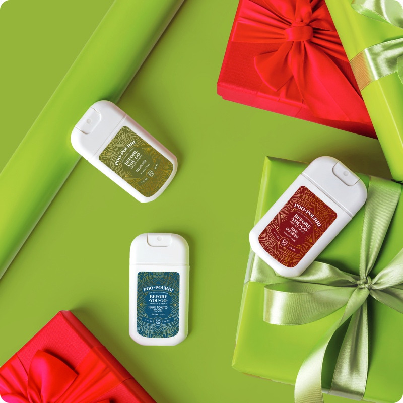 A festive arrangement featuring three Pocket Poo~Pourri sprayers on a vibrant green background, surrounded by elegantly wrapped red and green gift boxes with satin bows. The sprayers come in three scents: Enchanted Woods (green), Before You Go - Spiced Holiday (red), and Before You Go - Frosted Forest (blue). Perfect for on-the-go freshness, these pocket-sized sprays add a touch of luxury and holiday charm to any setting.