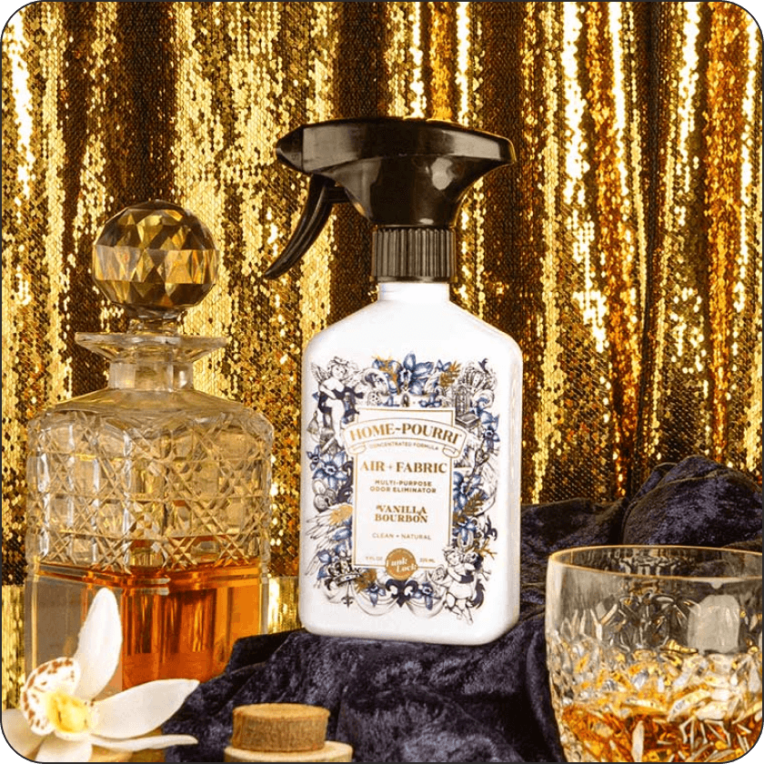 Home-Pourri Vanilla Bourbon air freshener bottle with decorative label, along with two glasses of bourbon with a gold curtain background