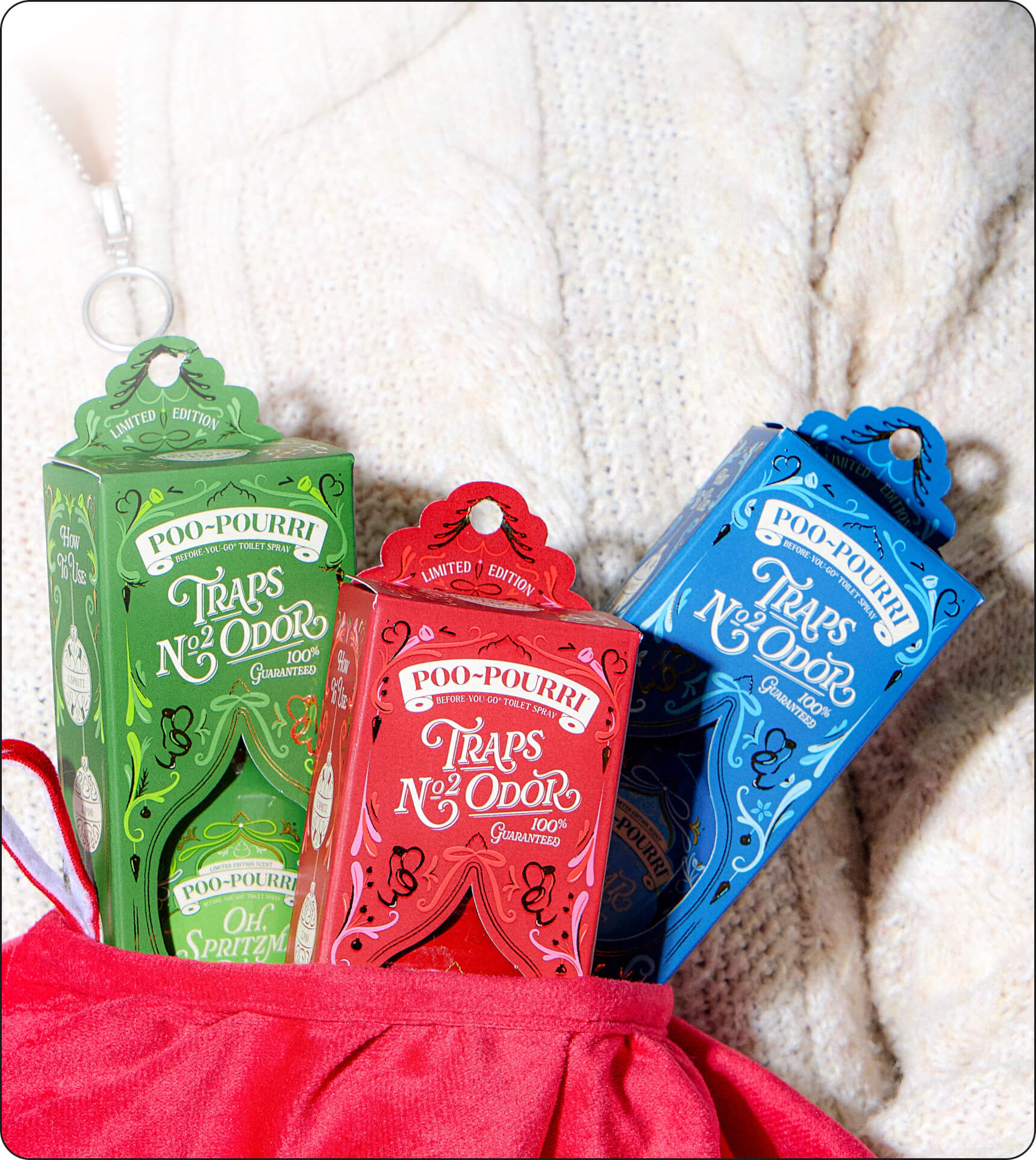 Three Poo-Pourri Holiday scents, arranged in a red fabric pouch on a white knit sweater.
