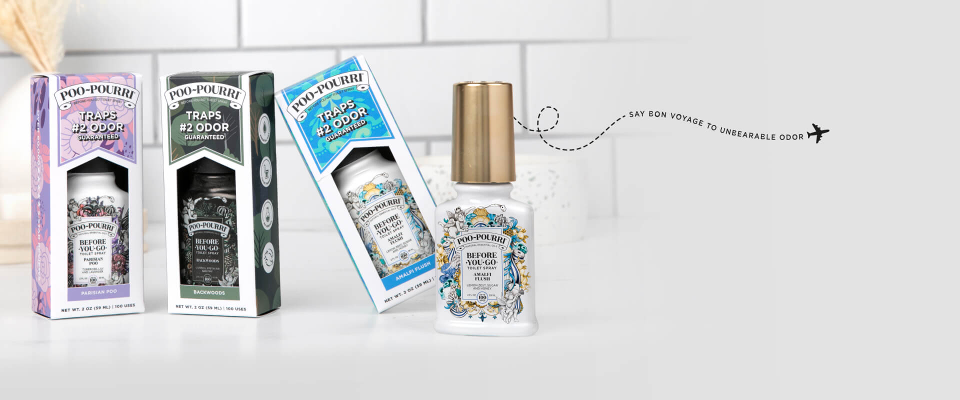 Three Poo-Pourri packages rest on a white tiled surface, offering the delightful scents of Parisian Poo, Backwoods, and Heaven Scent.