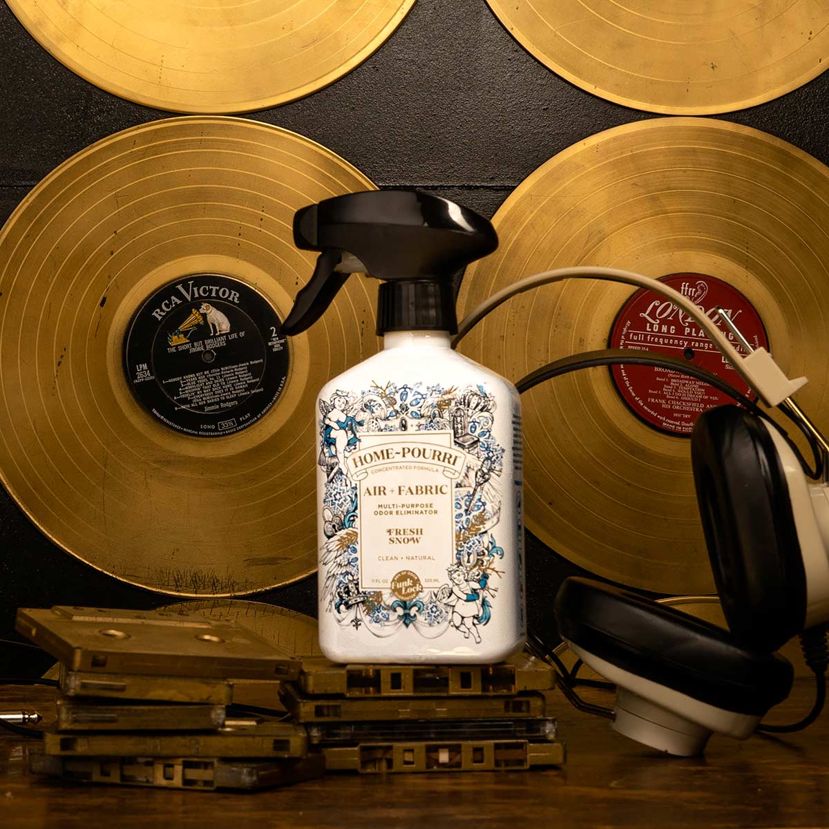 The Fresh Snow - Home~Pourri Room Spray by ~Pourri with Funk Lock Technology rests atop stacked tapes, surrounded by vinyl records and headphones against a dark backdrop.